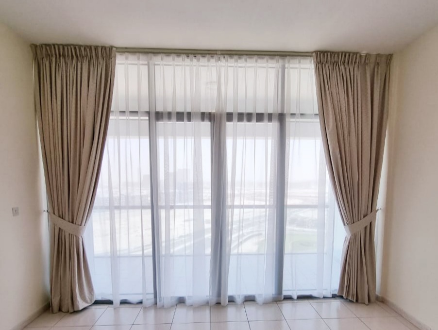 Freshly cleaned and repaired beige curtains with sheer drapes in a Dubai apartment living room